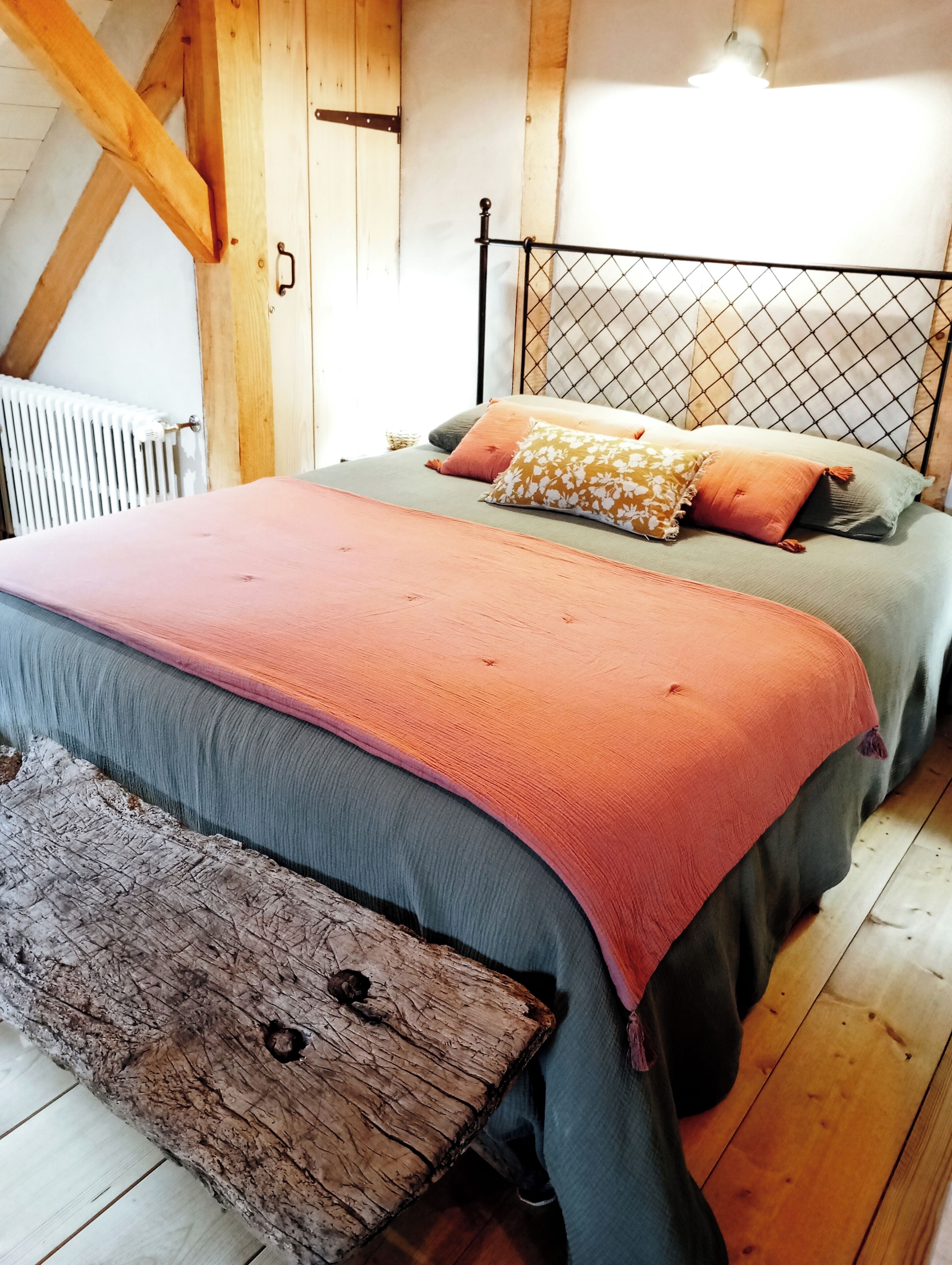 A wooden-framed room with a bed, a radiator, and a wooden bench.
