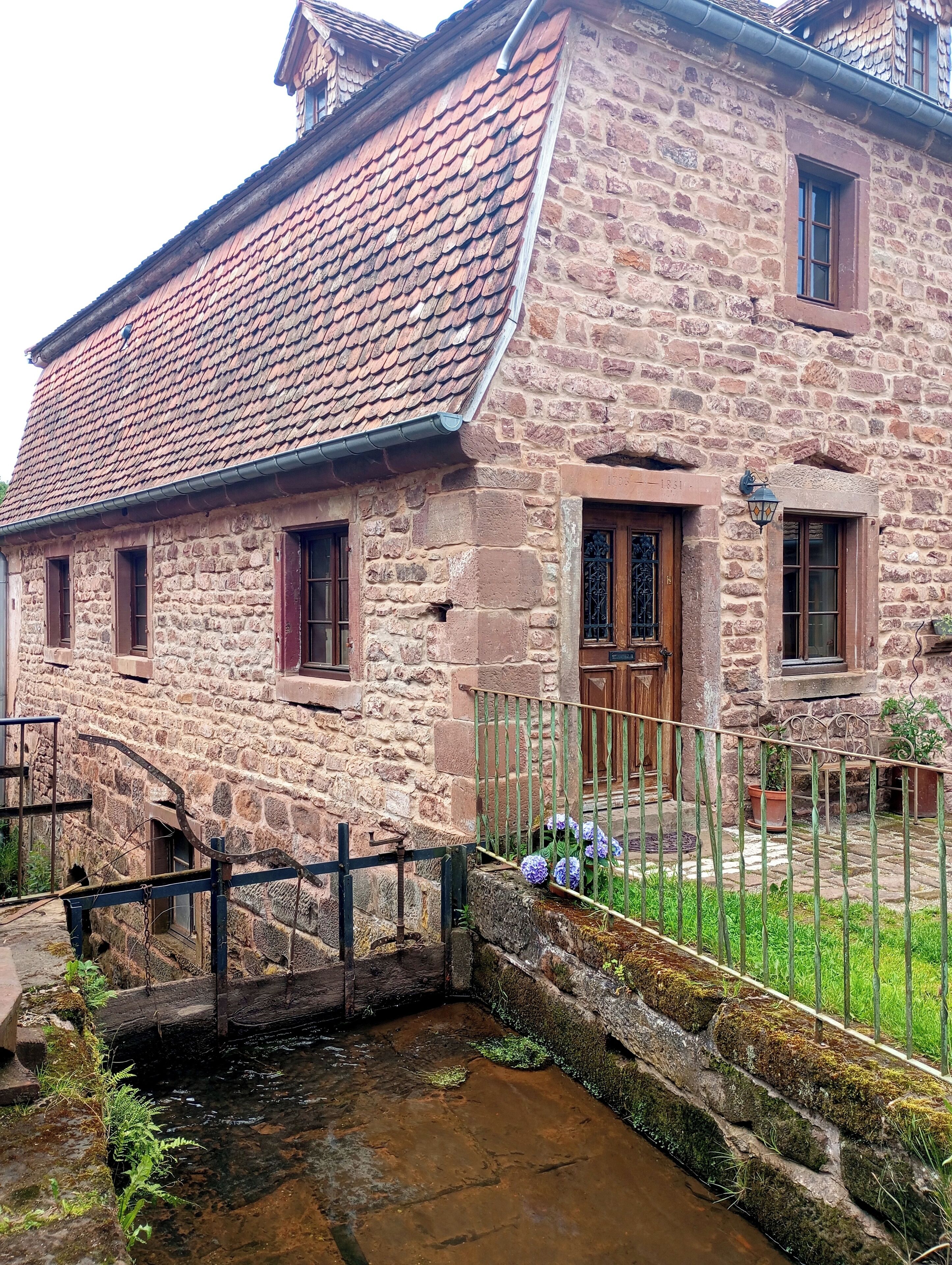 A stone building with a tiled roof, a wooden door, and a small window.