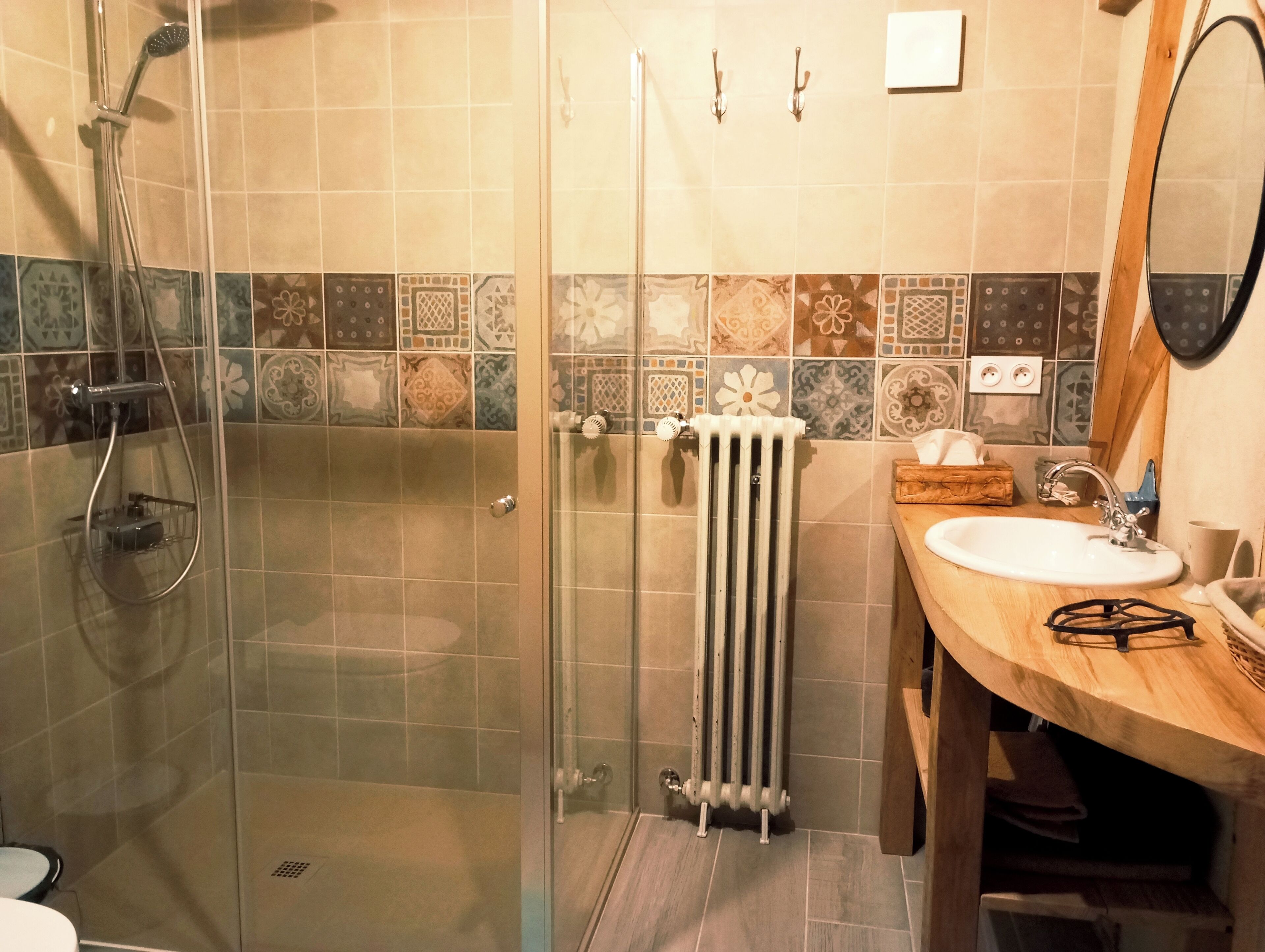 Ein Badezimmer mit einer ein Glasfachwerk-eingefassten Dusche, einem weißen Waschbecken, einem Holz-Waschtisch und einer gefliesten Rückwand.