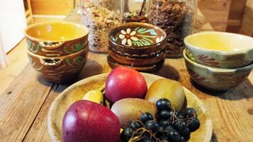 Una mesa de madera con un bol de frutas, incluyendo manzanas y uvas, y varios frascos de vidrio con granos y semillas.