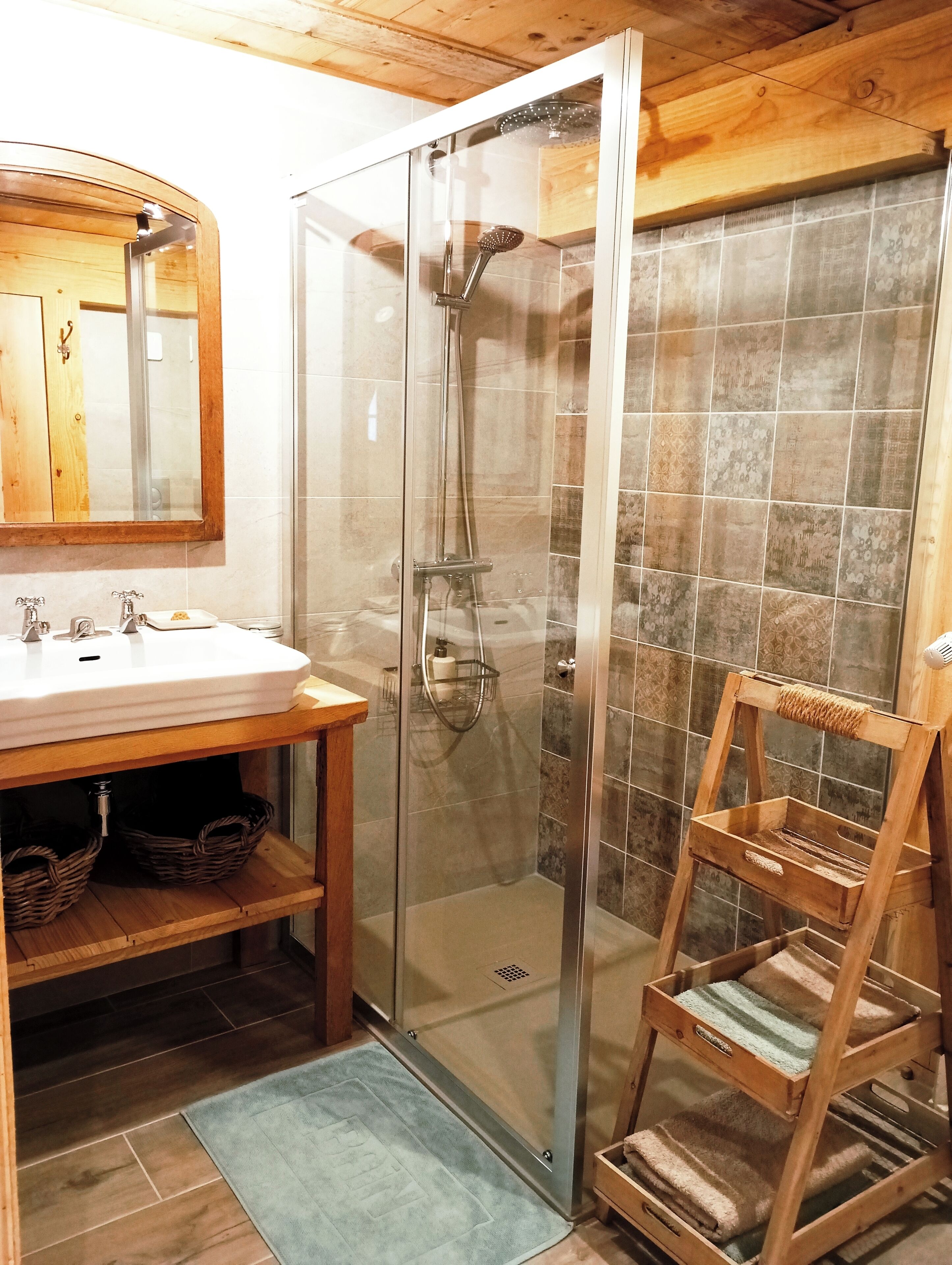 Un baño con ducha de vidrio, tocador de madera con lavabo y un perchero para toallas.