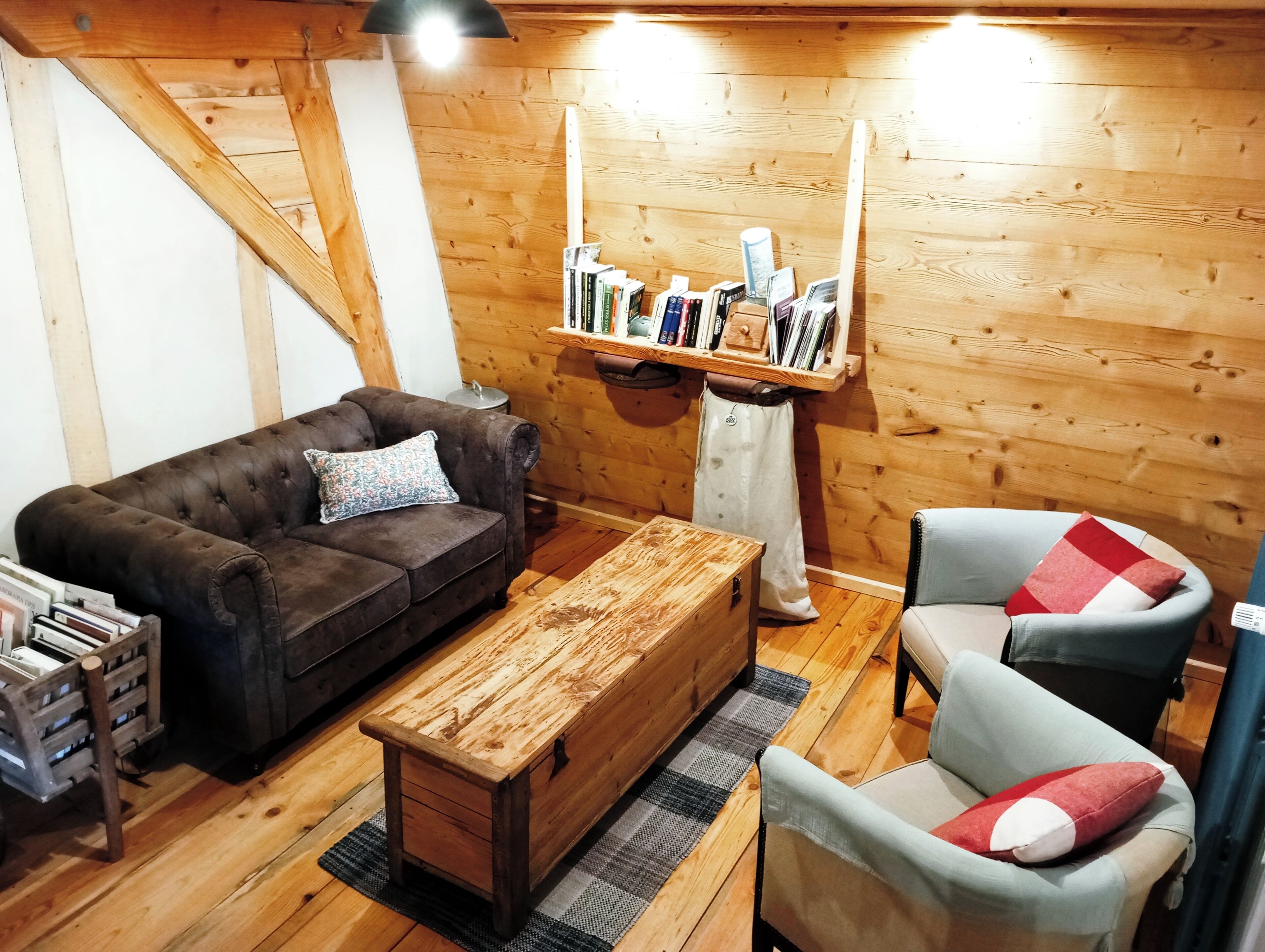A cozy living room with a brown sofa, a wooden coffee table, a grey armchair, and a bookshelf against the wall.