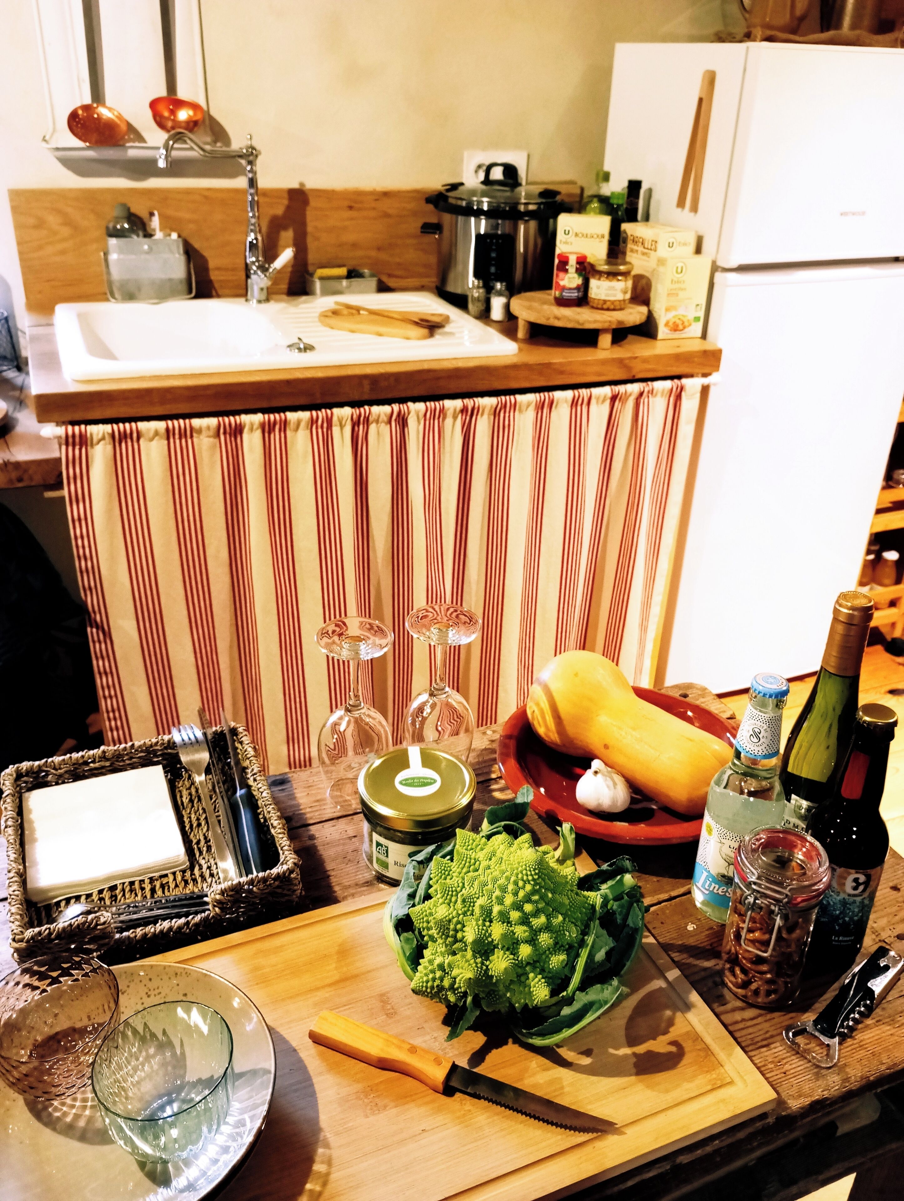A kitchen counter with a cutting board, knife, bottle, and various food items.