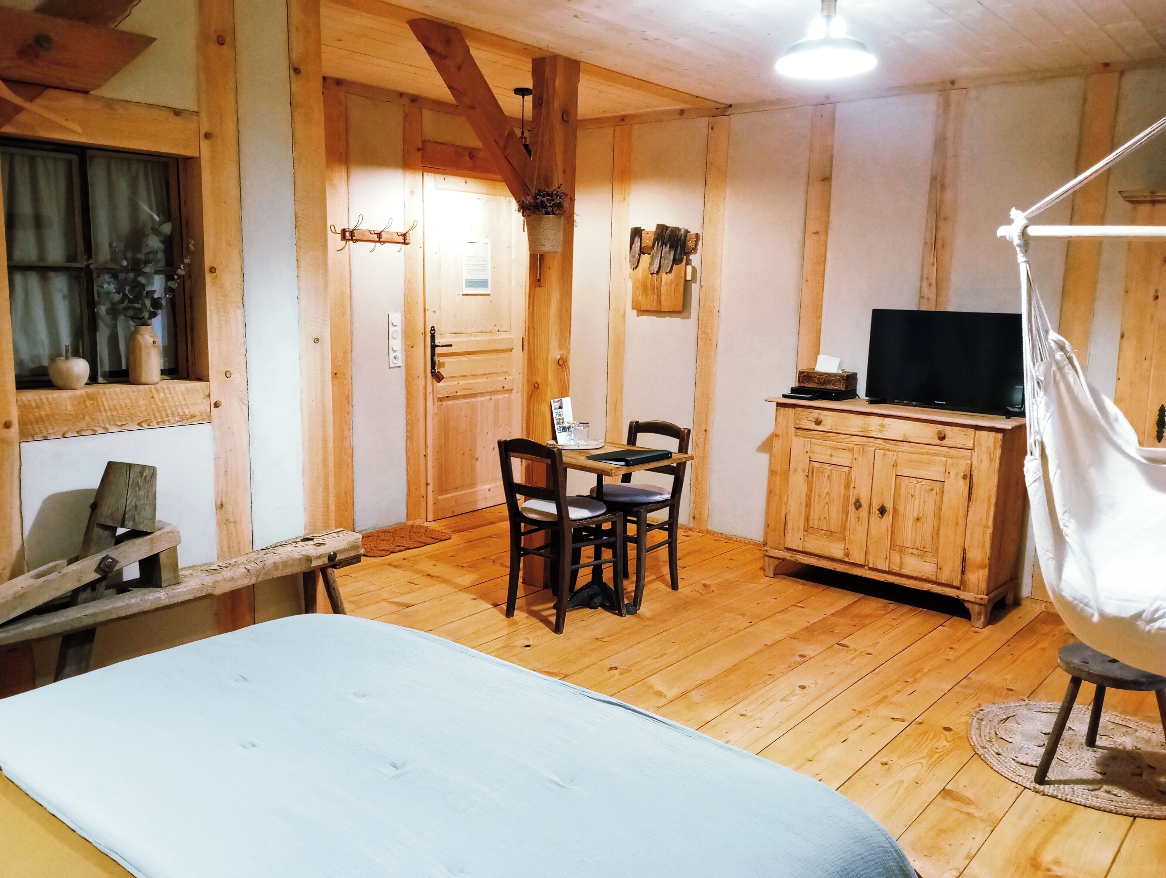 A wooden room with a bed, a table with chairs, a TV on a wooden cabinet, and a hanging chair.