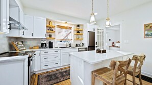 A modern kitchen with white cabinetry, a central island, wooden chairs, and pendant lighting.