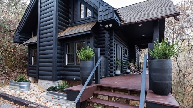 A log cabin with a wooden deck, large windows, and potted plants.