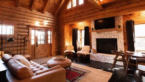 A log cabin interior with a stone fireplace, leather furniture, and a TV mounted on the wall.