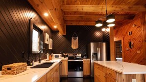 A modern kitchen with wooden walls, a stainless steel refrigerator, a microwave, and a sink.