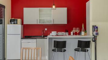 Cocina compacta con pared roja, gabinetes blancos, microondas integrado y una barra con dos taburetes.