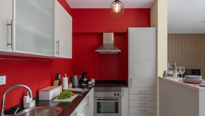 A modern kitchen with red walls, stainless steel appliances, and a white countertop. - Vacation Home in Porto Santo, Villa Girassol (Porto Santo)