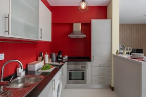 A modern kitchen with red walls, stainless steel appliances, and a white countertop. - Vacation Home in Porto Santo, Villa Girassol (Porto Santo)