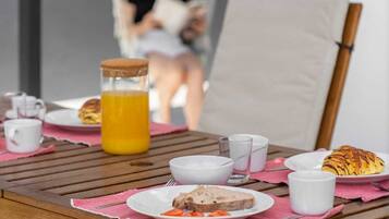 A wooden table with breakfast items, including bread, a croissant, and a glass of orange juice.
