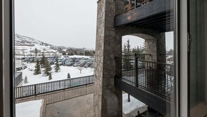 A multi-level building with stone pillars, balconies, and a view of a snowy parking lot with trees.