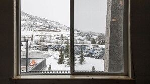 A view through a window of a snowy landscape with a parking lot, trees, and buildings in the background.