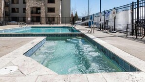 A swimming pool with a stone facade, surrounded by a metal fence, and adjacent to a multi-story building.