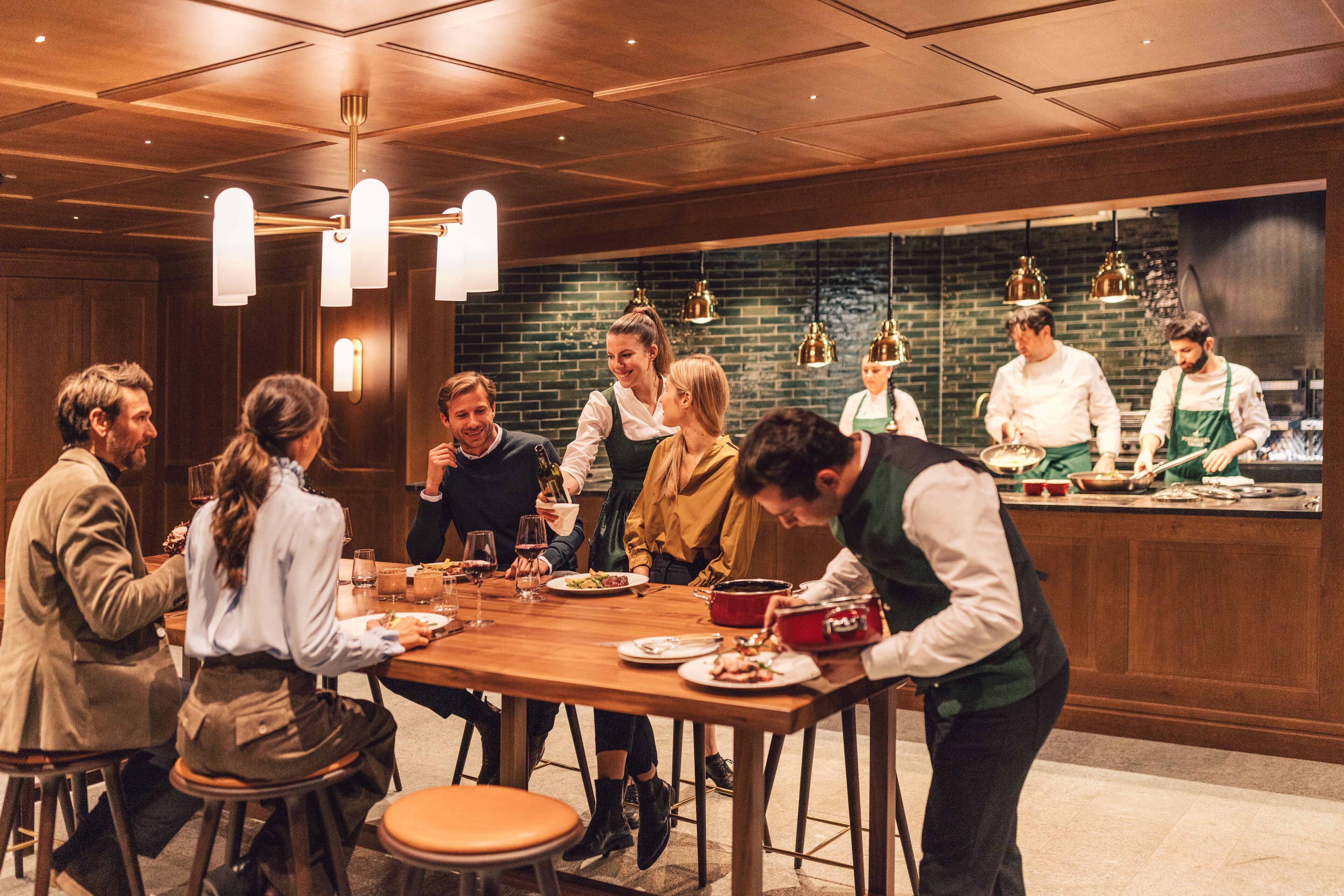 A group of people dining at a restaurant with a wooden interior and hanging pendant lights.