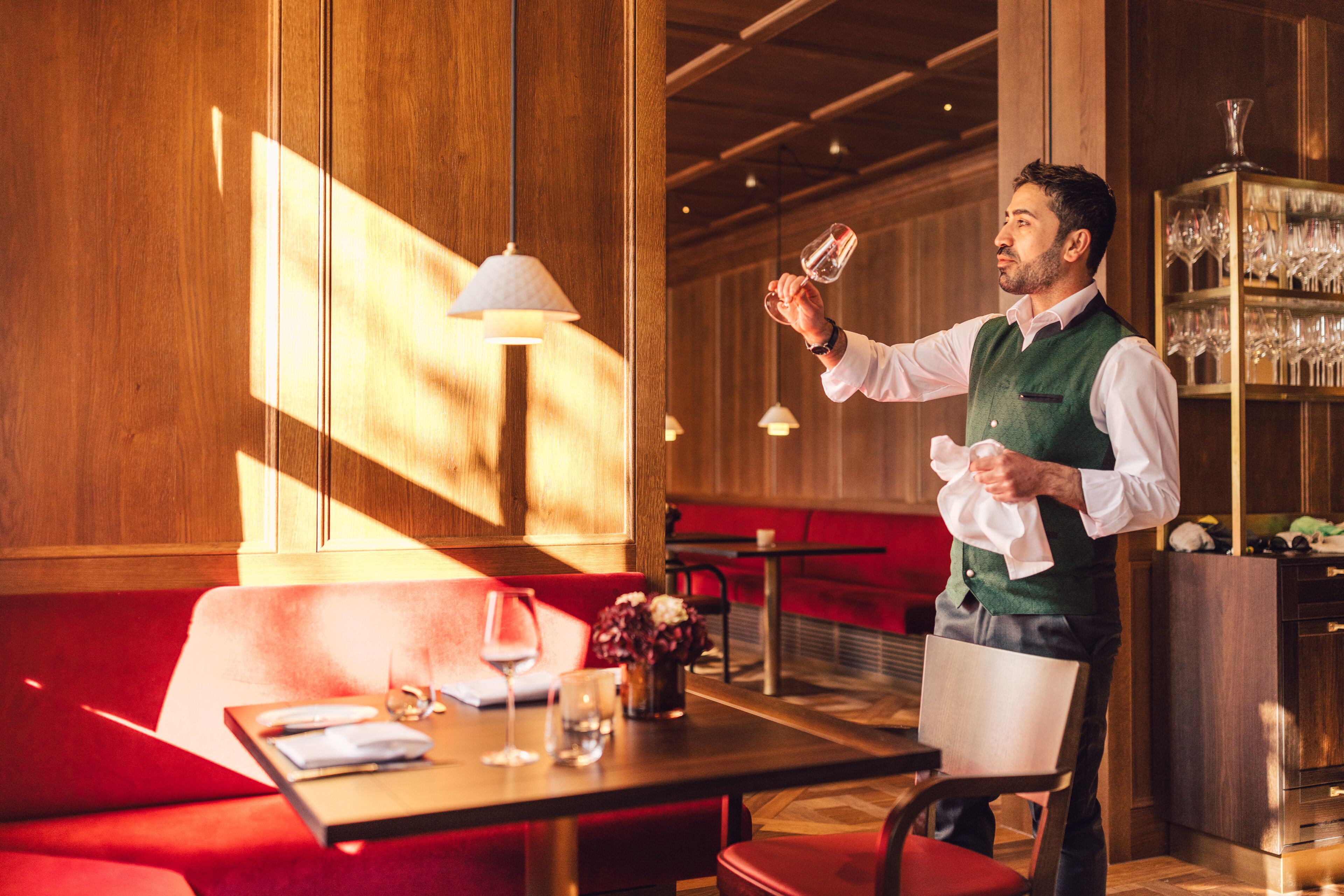 L’intérieur d’un restaurant, avec des lambris en bois, un coin salon avec des banquettes rouges et un bar où l’on peut voir des verres.