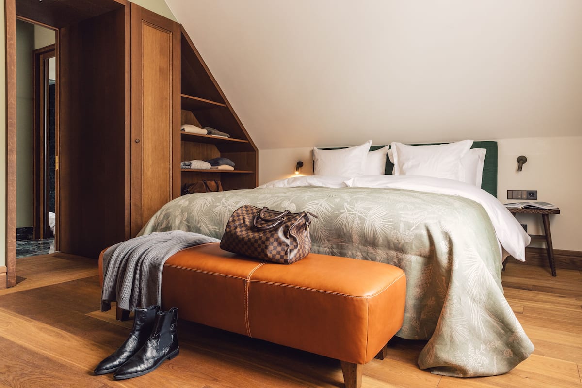 Un dormitorio con una cama, un armario de madera, un banco y un bolso.