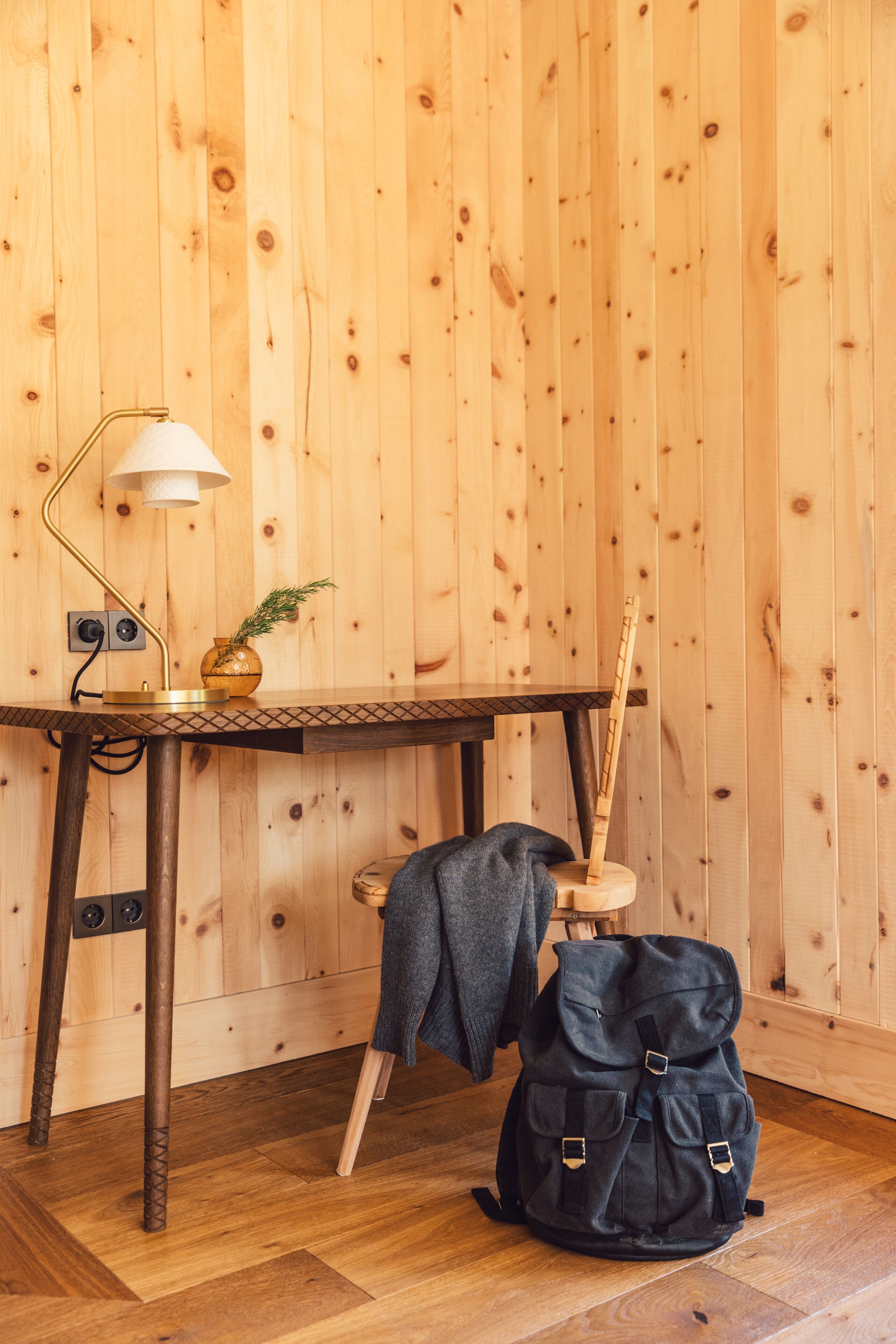 Um quarto de madeira com uma escrivaninha, luminária e uma mochila.