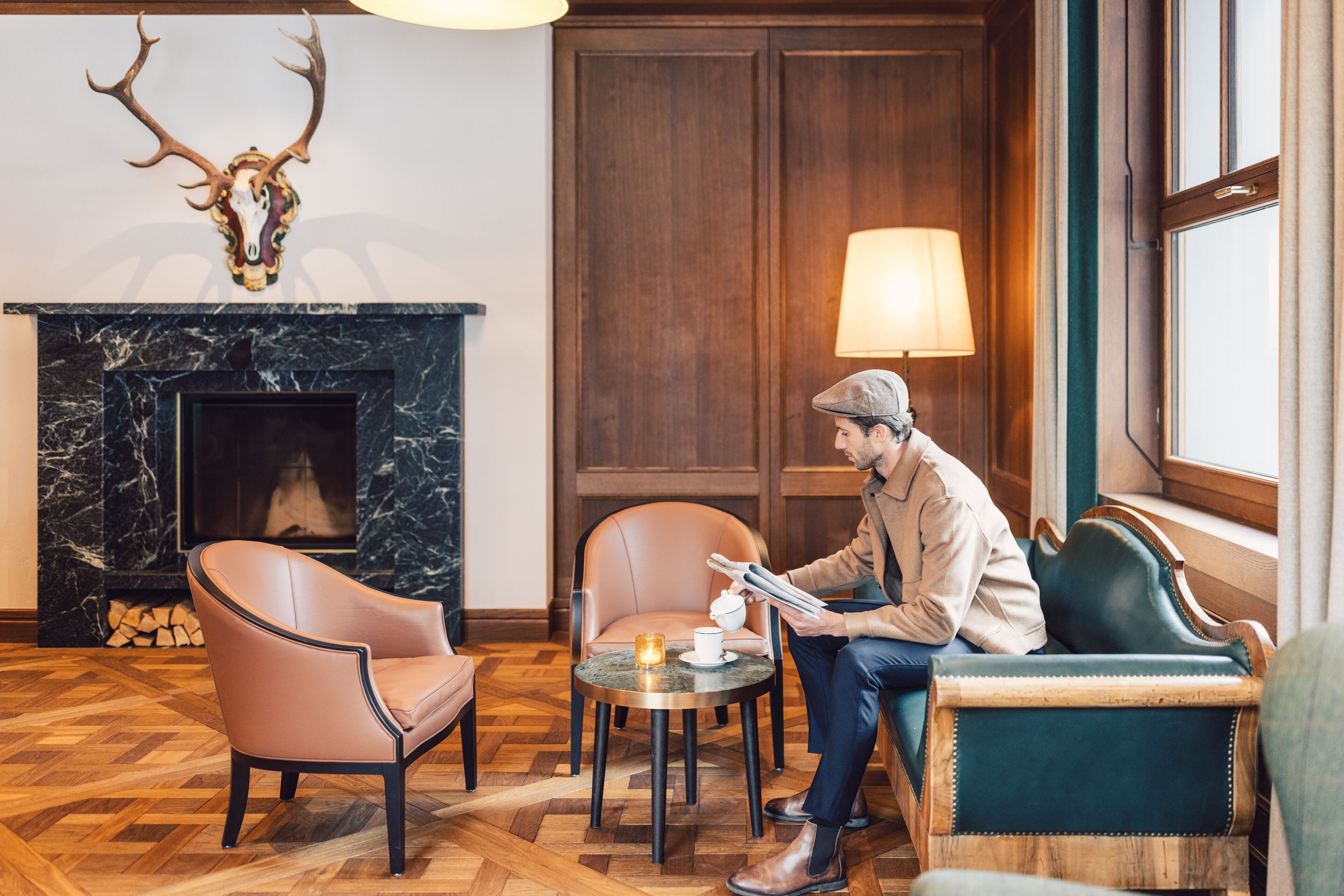 Een kamer met een open haard, leren fauteuils, een tafel met een kaars en een persoon die leest.