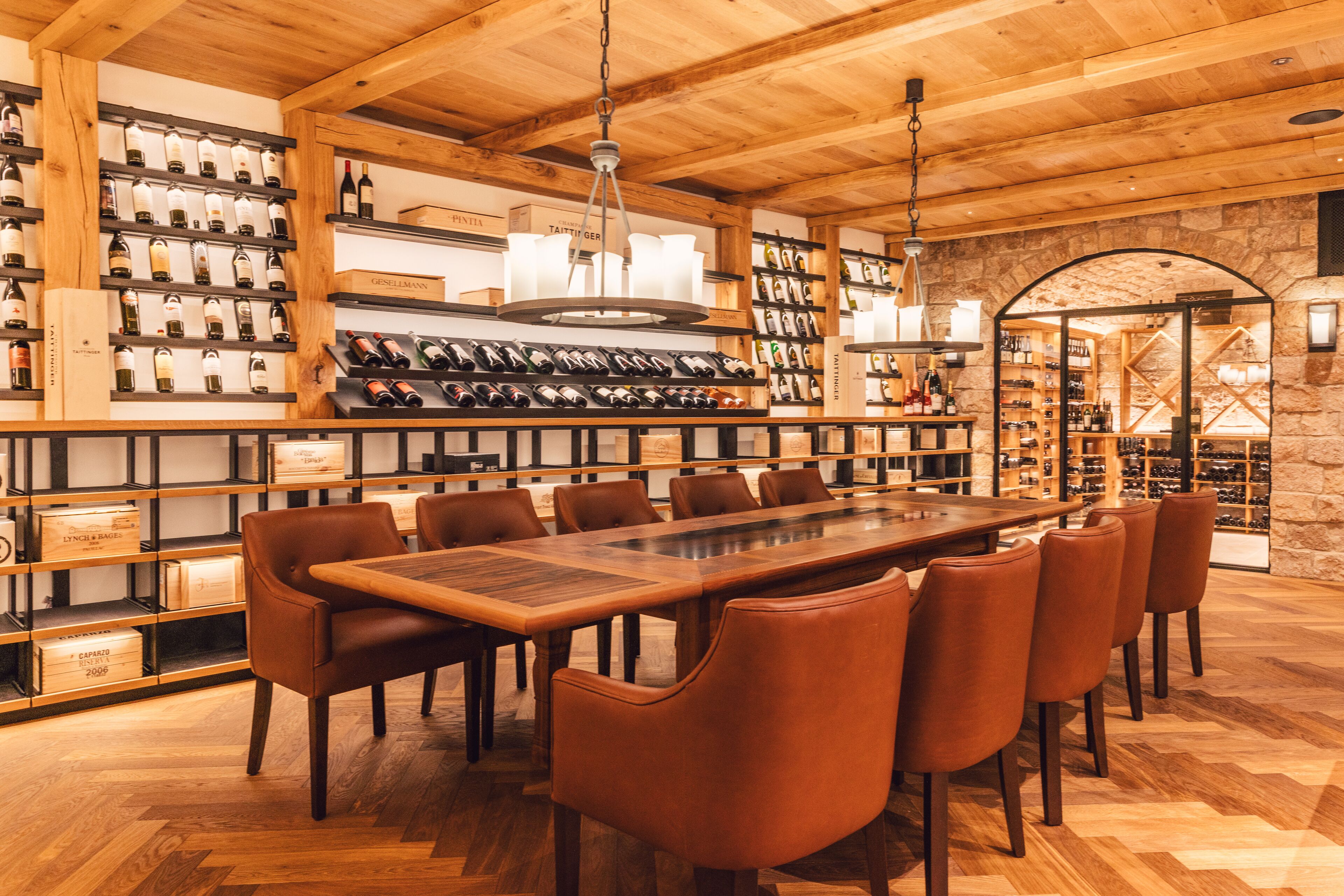 Un restaurante con una larga mesa de madera y sillas de cuero, rodeado de estantes llenos de botellas de vino.