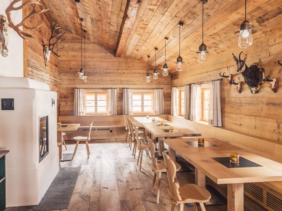 A rustic wooden interior with long tables and chairs, wooden ceiling beams, and mounted animal skulls.