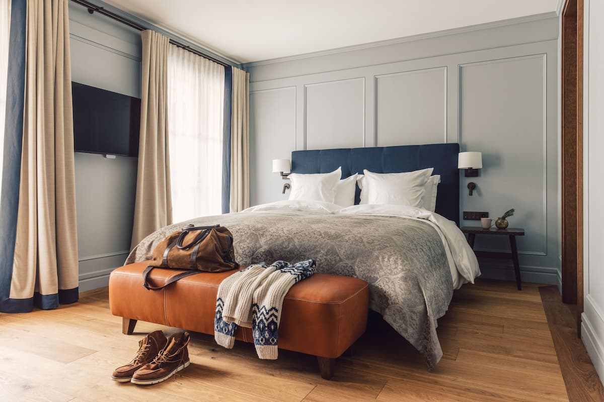 Un dormitorio con una cama, una mesita de noche, una lámpara, un televisor y una ventana con cortinas.