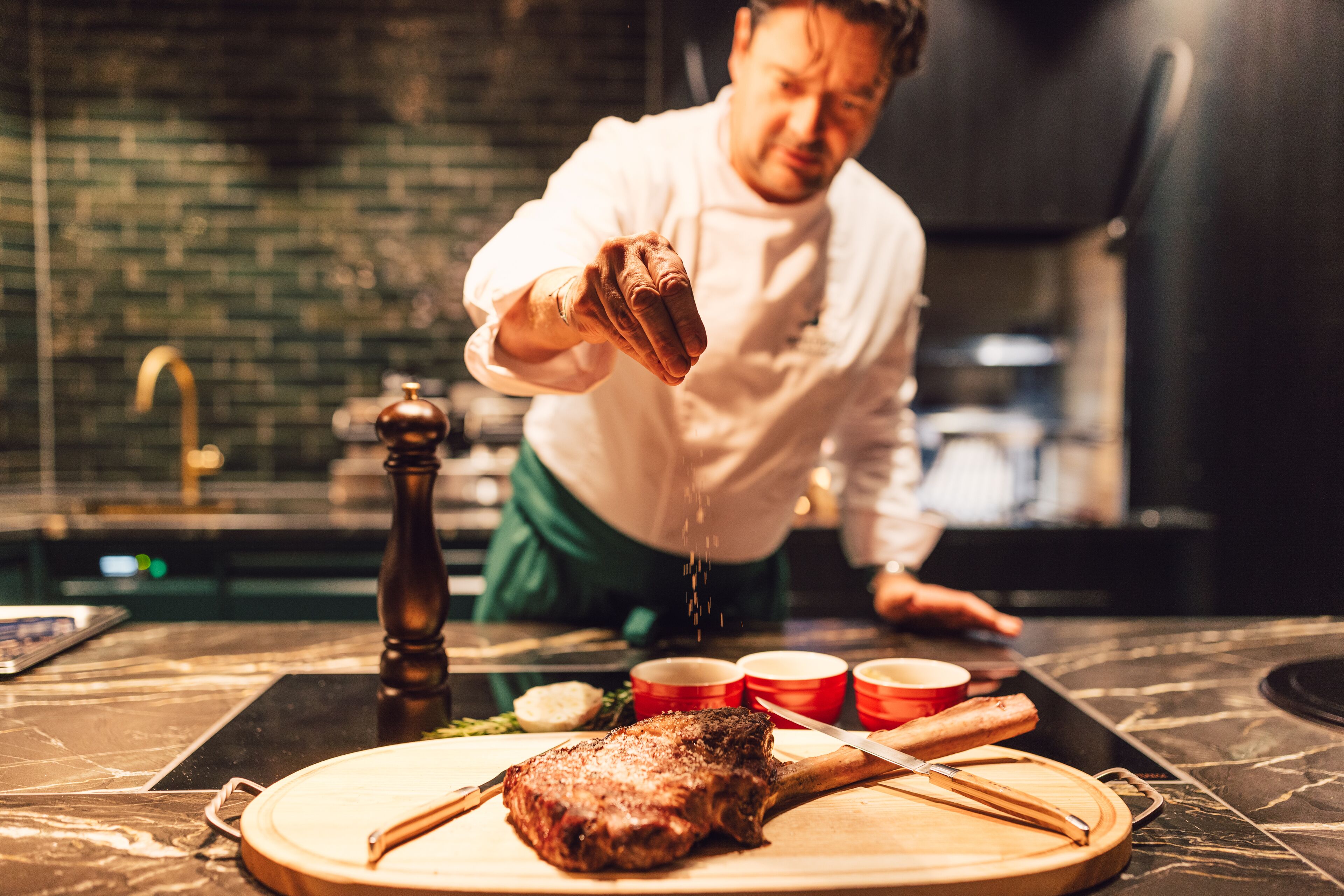 Un chef sazona un bistec sobre una tabla de cortar en una cocina.
