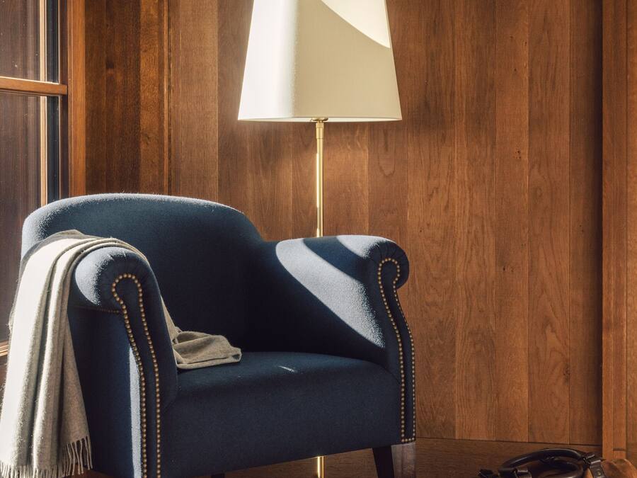Ein Zimmer mit einem dunkelblauen Sessel, einer weißen Stehlampe und einer braunen Tasche auf dem Boden.