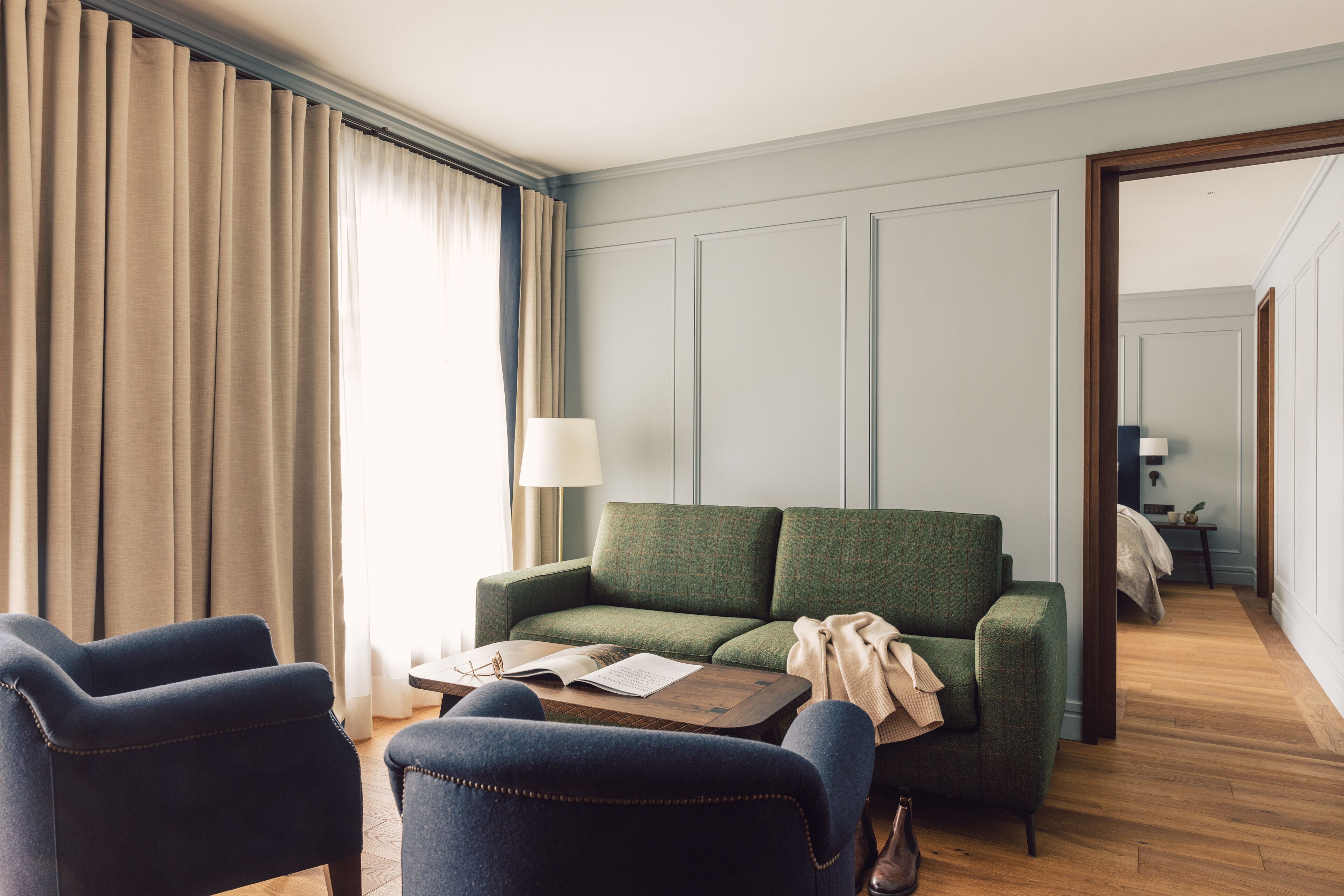 A hotel room with a green sofa, two armchairs, a wooden coffee table, and a lamp.