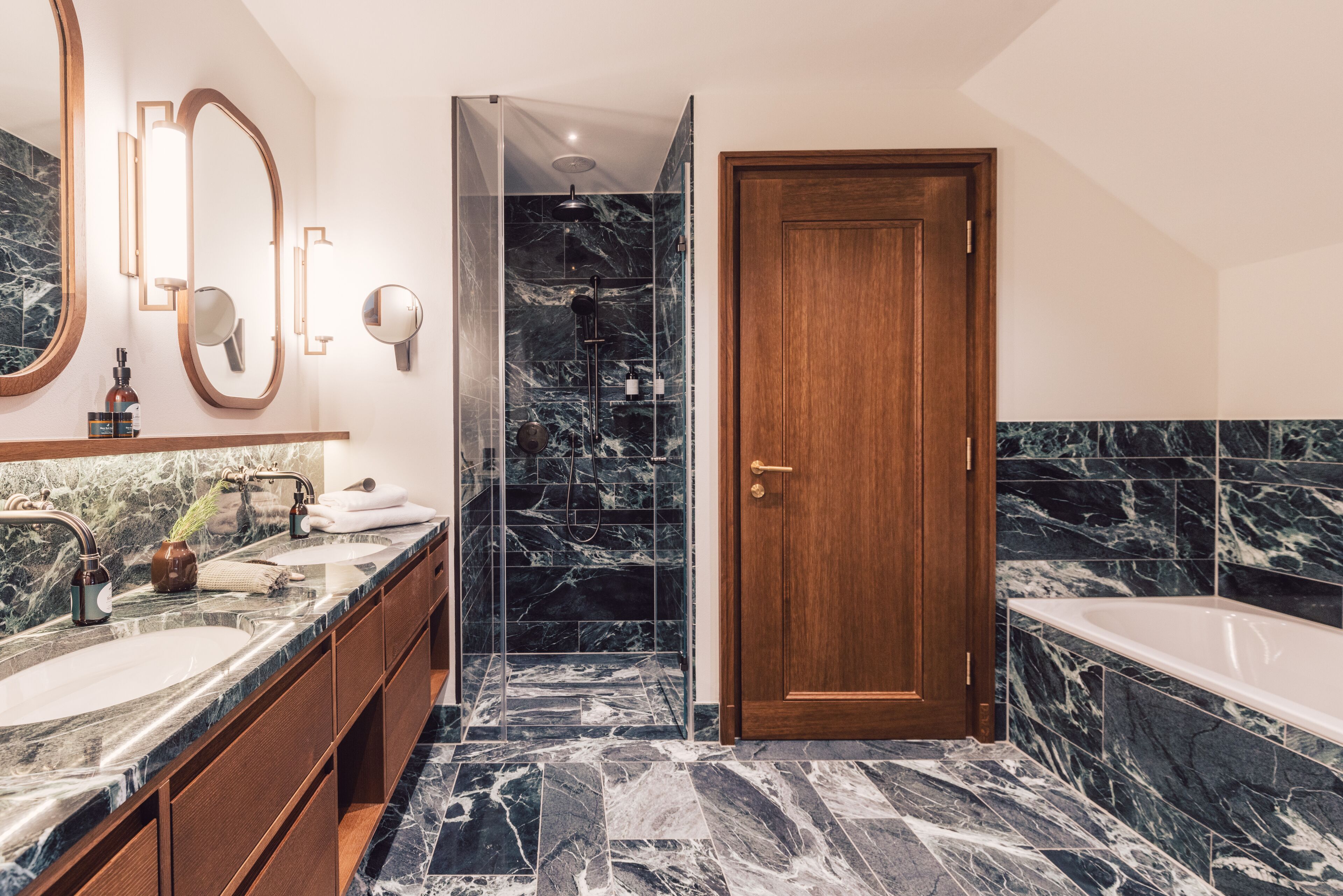 A modern bathroom with a marble vanity, a separate shower area, and a wooden door.