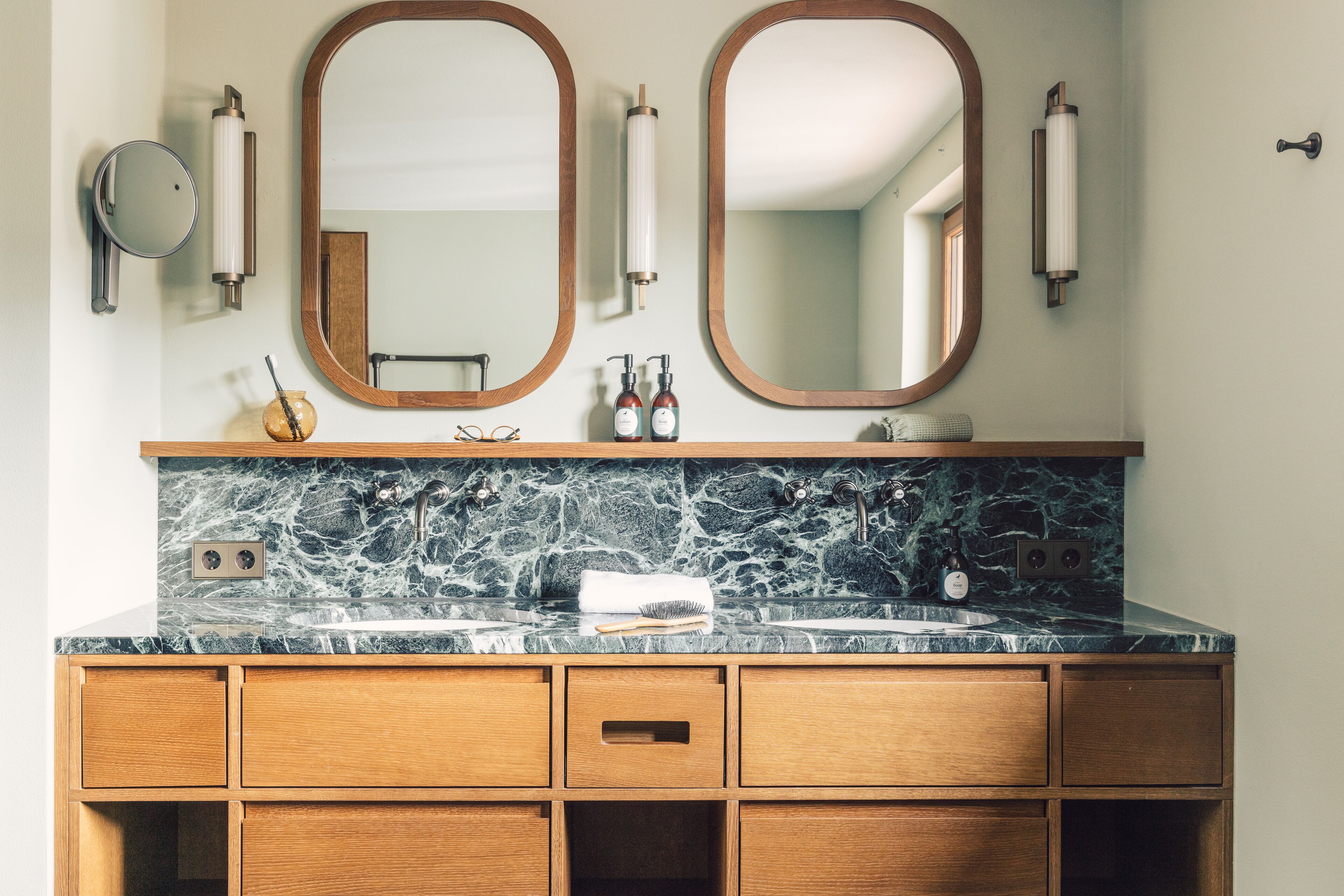 A bathroom with a marble countertop, wooden vanity, two mirrors, and a towel rack.