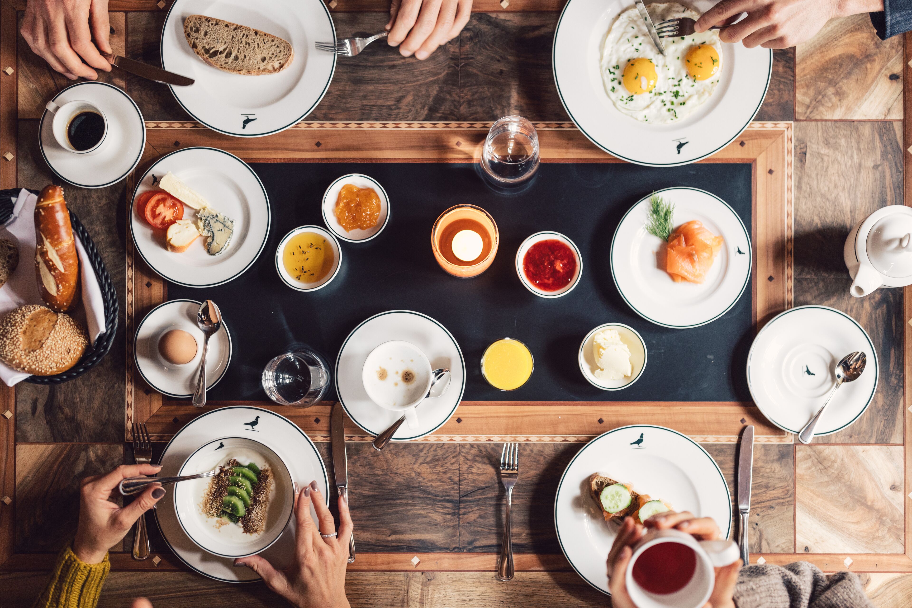 Un desayuno con diversos platos, utensilios y una vela en el centro de una mesa de madera.