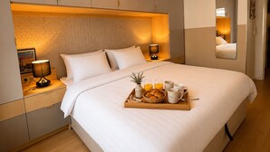 Een hotelkamer met een groot bed, nachtlampjes, een dienblad met ontbijtartikelen en een spiegel aan de muur.