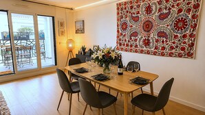 Een eethoek met een tafel voor vier personen, stoelen, een vaas met bloemen, een wijnfles en een lamp.
