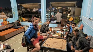 A group of people playing foosball on a table in an outdoor seating area with a city view. - Madpackers Udaipur (Udaipur)