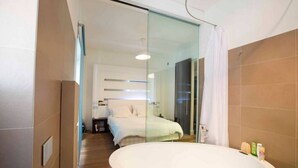 A modern hotel room with a large bathtub, a glass partition, a bed with white bedding, and a small bedside table. - Entire apartment in Ravda (Ravda, Nessebar community)