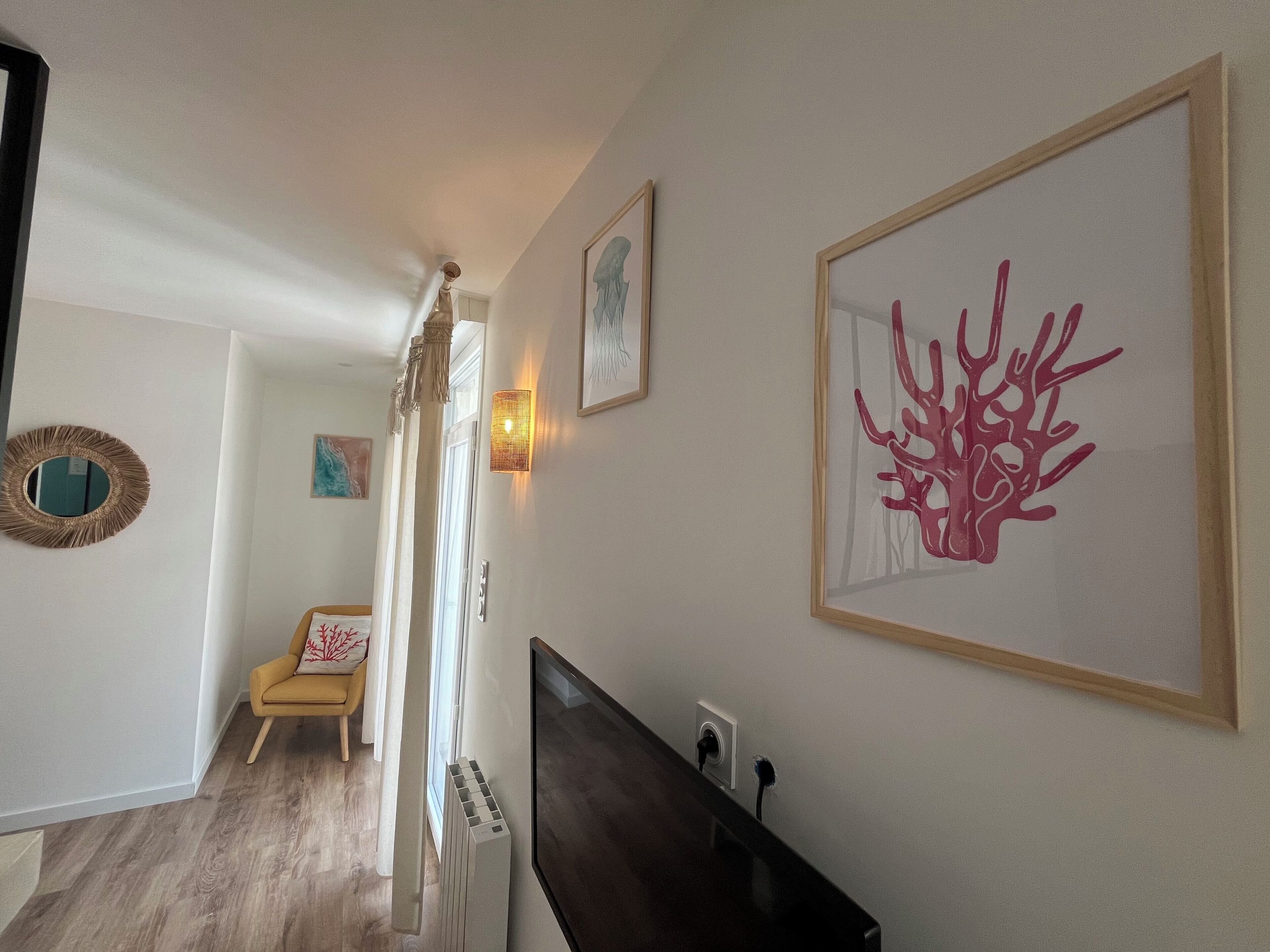 Un pasillo con un radiador, una obra enmarcadas de coral y una silla con estampado de hojas rojas.