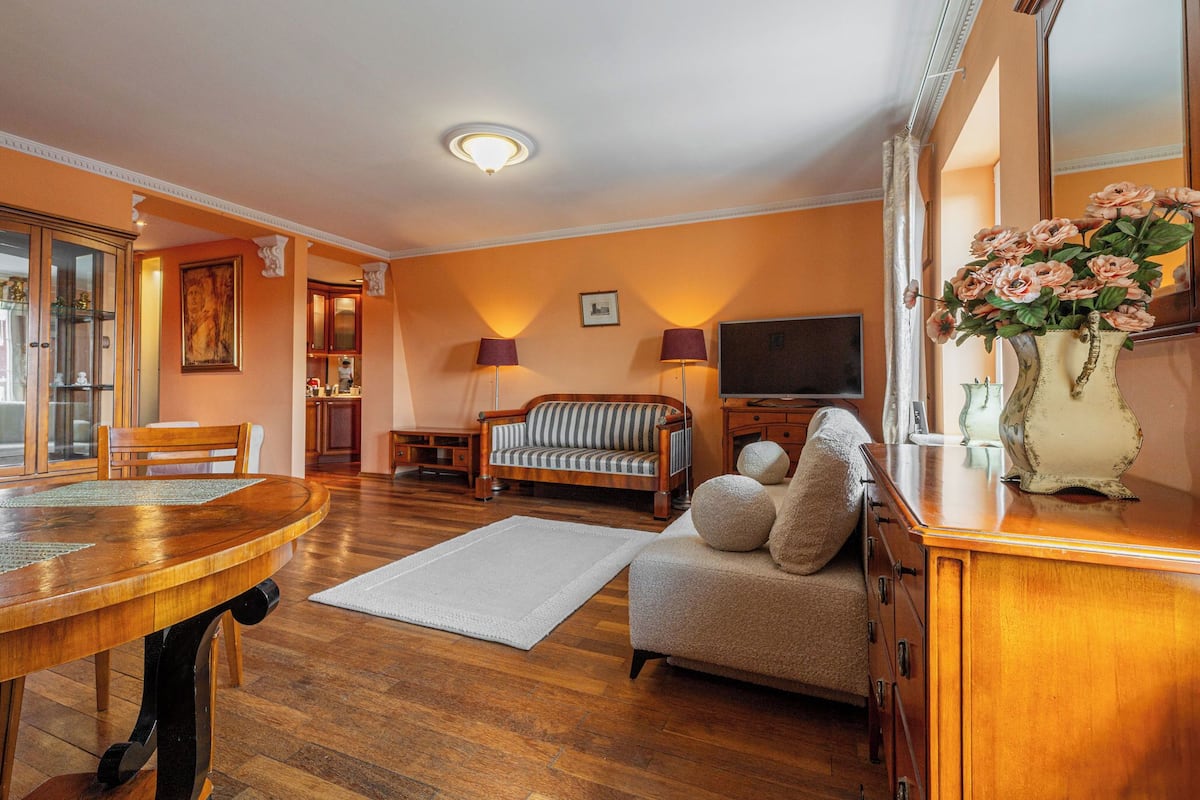 Una sala de estar con una mesa de comedor de madera, un sofá, un televisor y un florero con flores.