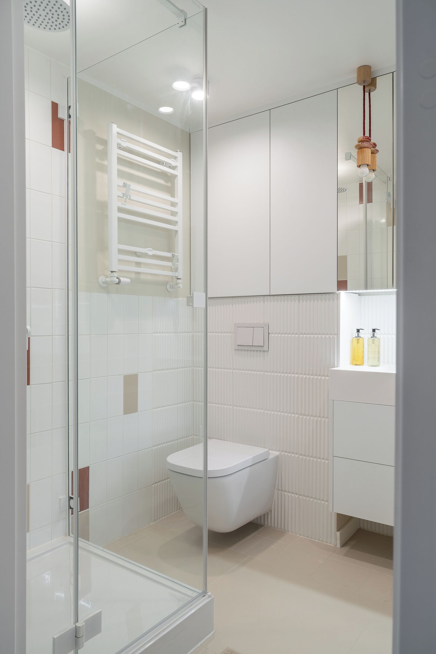 Un baño moderno con cabina de ducha de vidrio, inodoro blanco y estante empotrado con artículos de aseo.