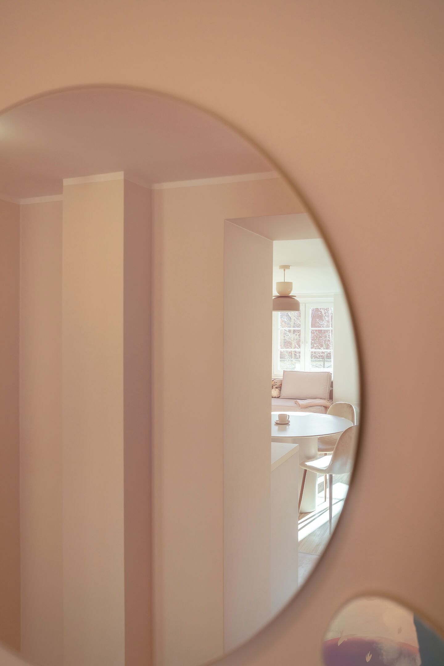 A circular mirror reflecting a room with a bed, a window, and a hanging light fixture.