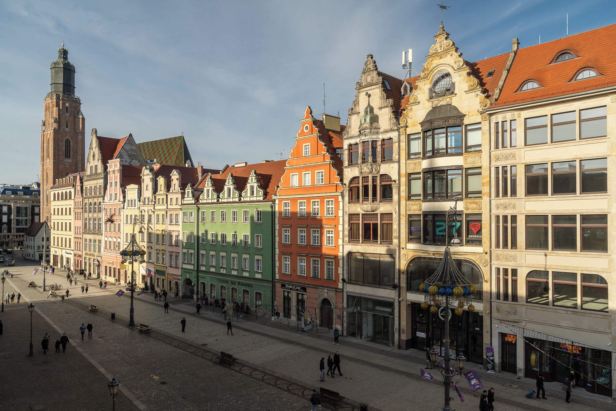 A historic European street with colorful buildings, a prominent church tower, and a tram line.