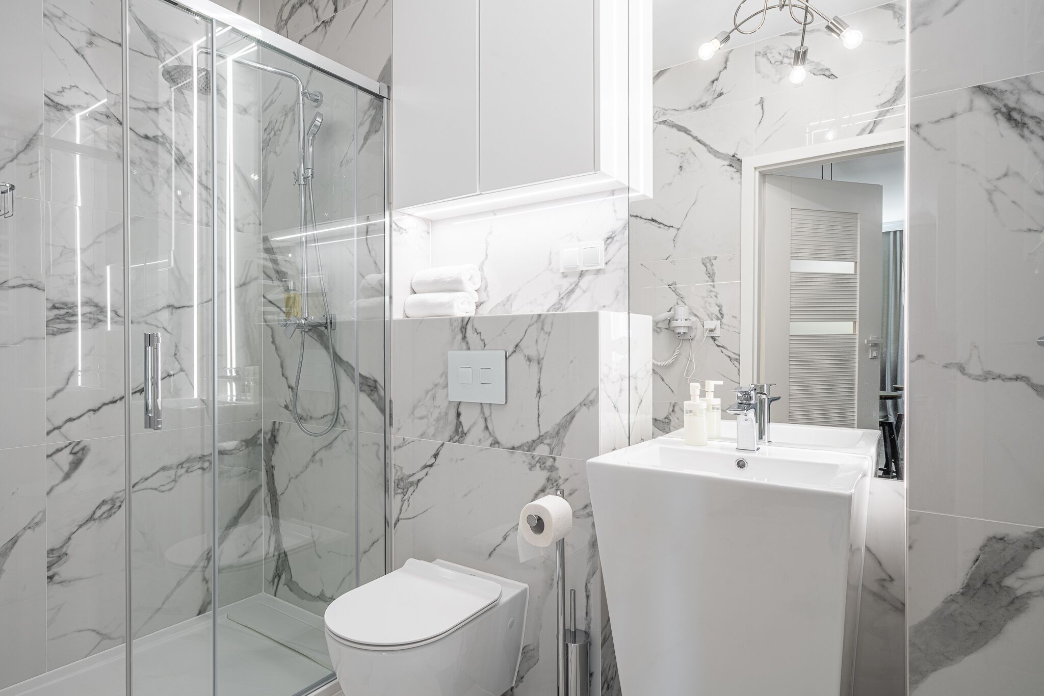 Een moderne badkamer met een glazen douchecabine, een wit toilet en een wastafel met spiegel erboven.