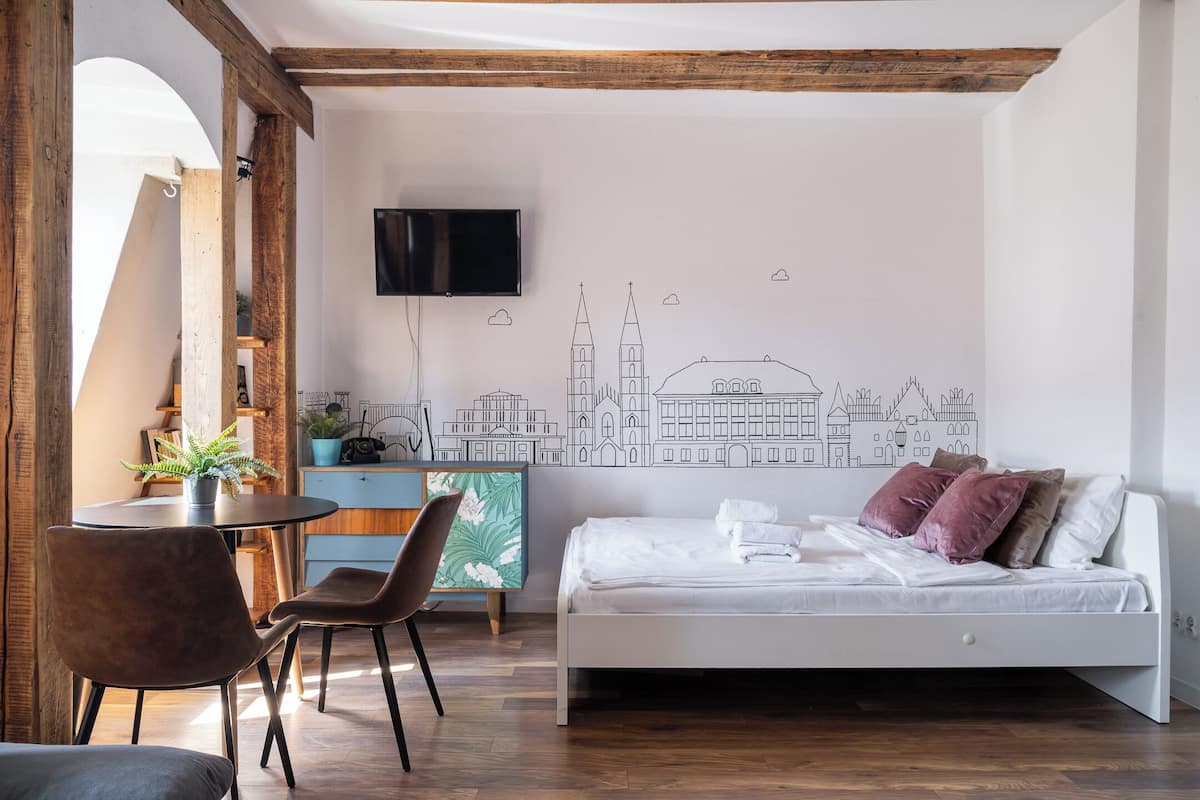 Un dormitorio moderno con una cama, un escritorio, sillas y un mural con un paisaje urbano en la pared.