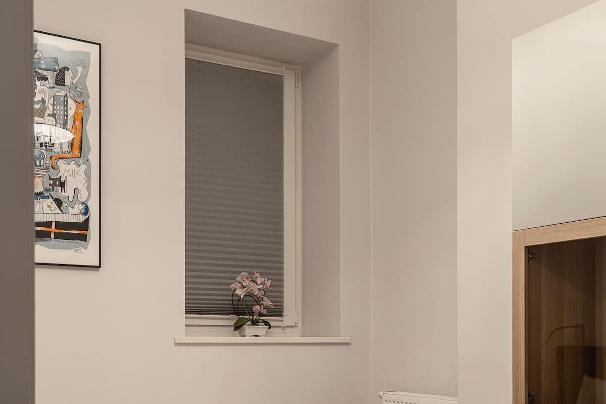 Un dormitorio con una cama individual, una ventana con persianas, un radiador y un cuadro en la pared.