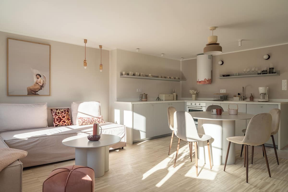 Una sala moderna con un sofá, una mesa de centro redonda y un comedor con sillas. Hay una cocina con estufa, lavaplatos y estantes sobre la encimera.