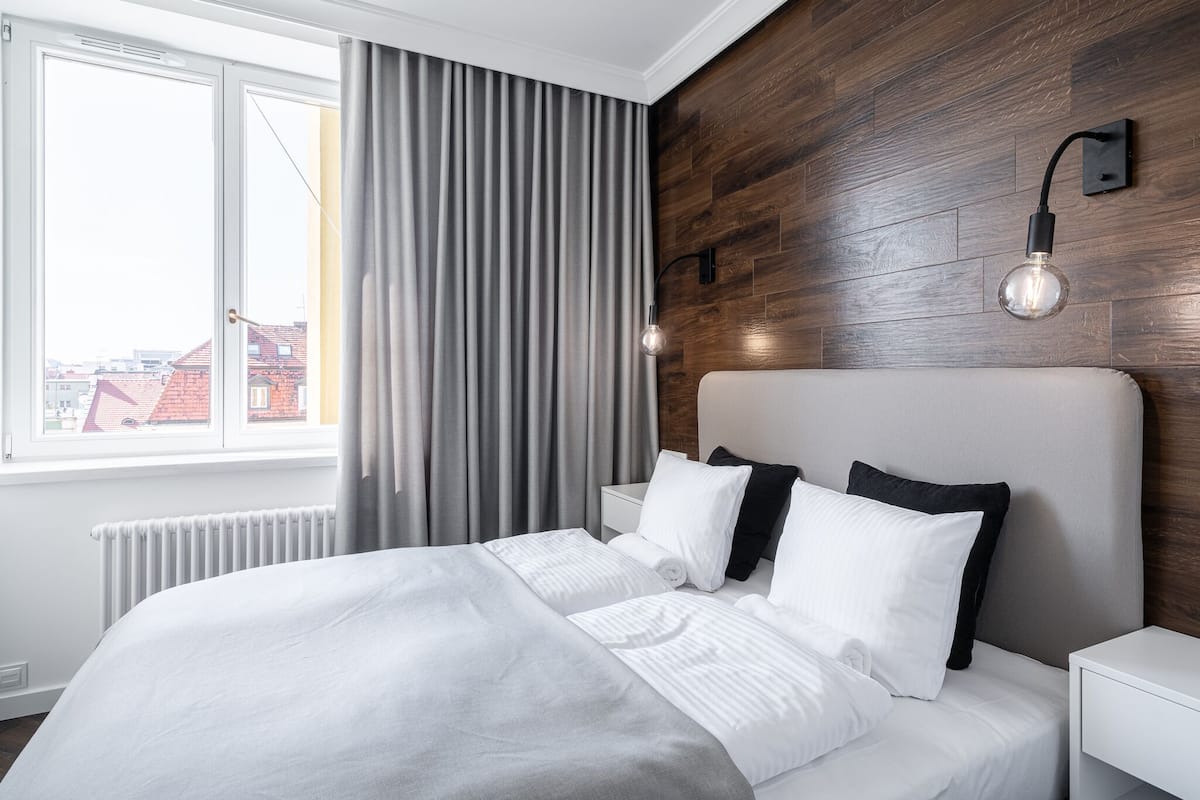 Una habitación de hotel moderna con una cama grande, una pared de acento de madera, una ventana con cortinas y una lámpara fijada a la pared.