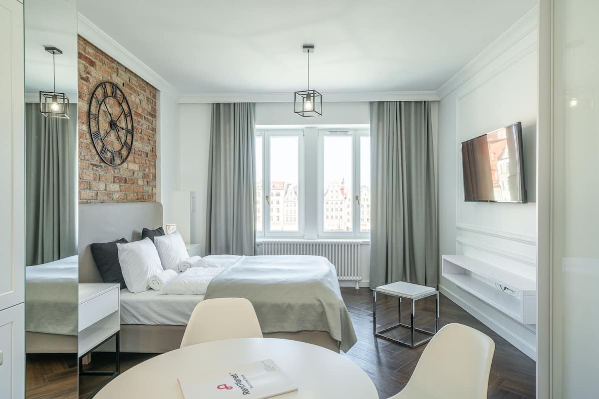 Habitación de hotel moderna con una pared de ladrillo decorativa, una cama grande, una mesita pequeña y un televisor montado en la pared.