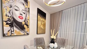 Uma área de refeições com uma mesa de vidro rodeada por quatro cadeiras, uma luminária pendente moderna e duas obras de arte na parede.