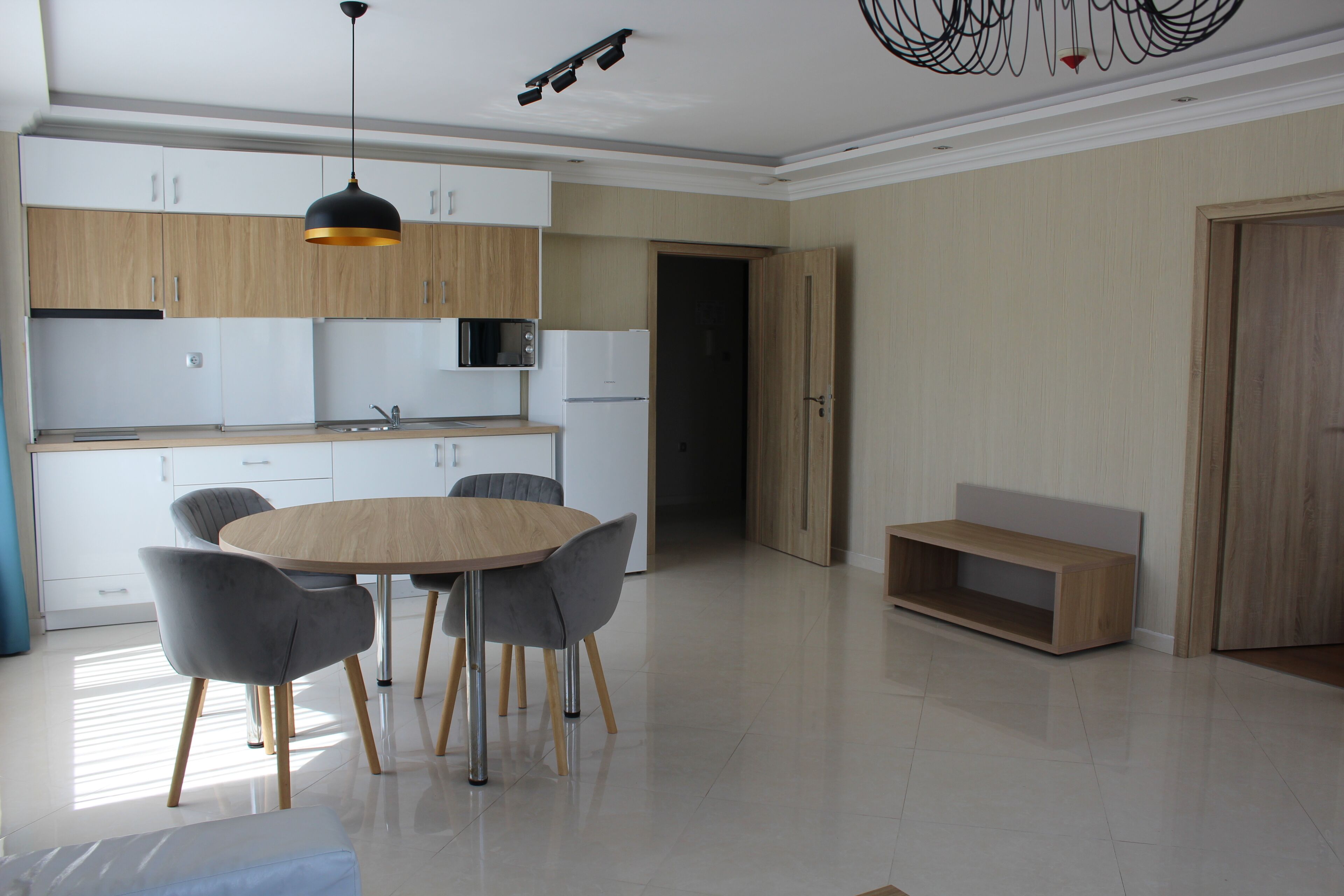 A modern kitchen with a round dining table, grey chairs, and wooden cabinets.
